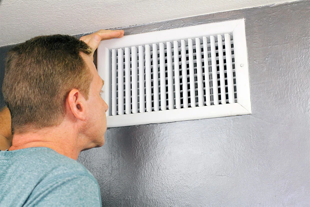 A man looking at a vent in a room.