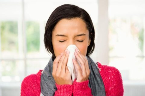 A woman blowing her nose with a tissue.