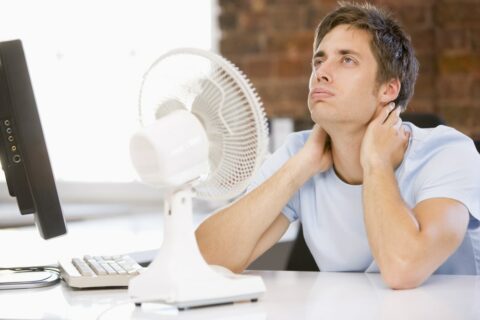 A man sitting at his desk with a fan on his neck.