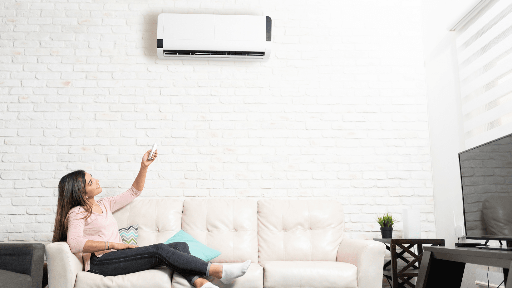 A woman sitting on a couch next to an air conditioner.