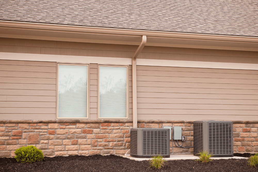 A house with two air conditioners in front of it.