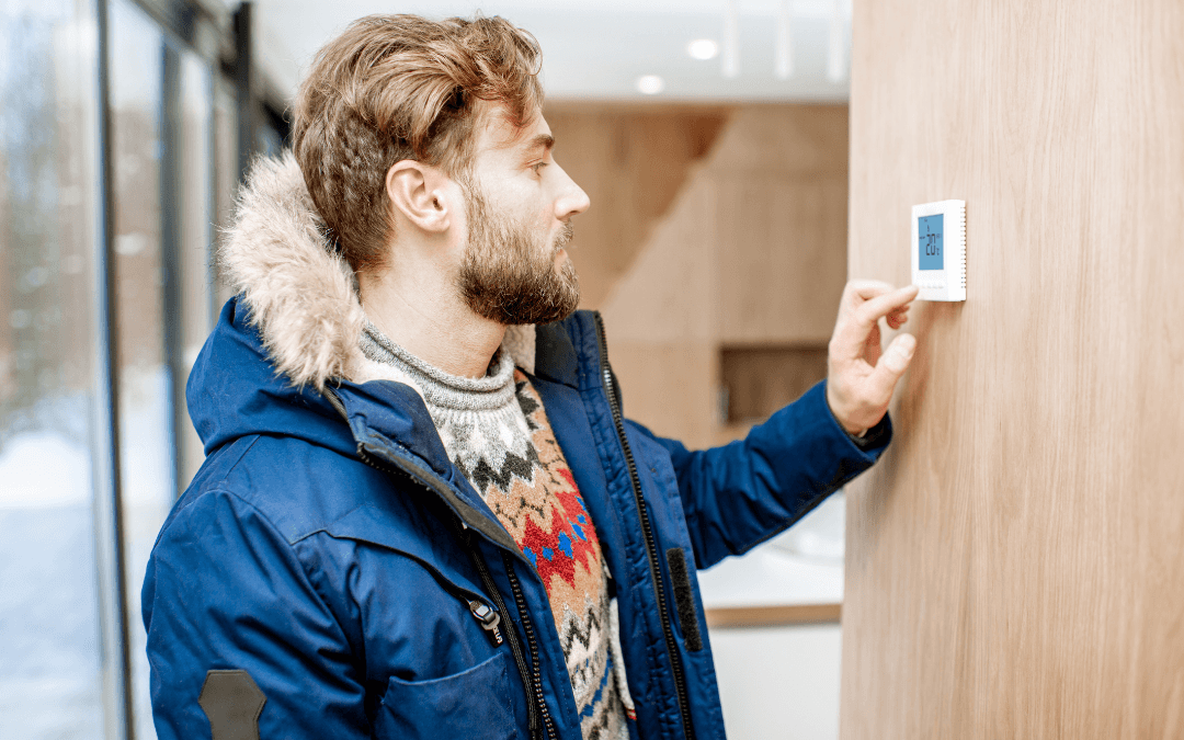 A man in a winter jacket is looking at a thermostat.