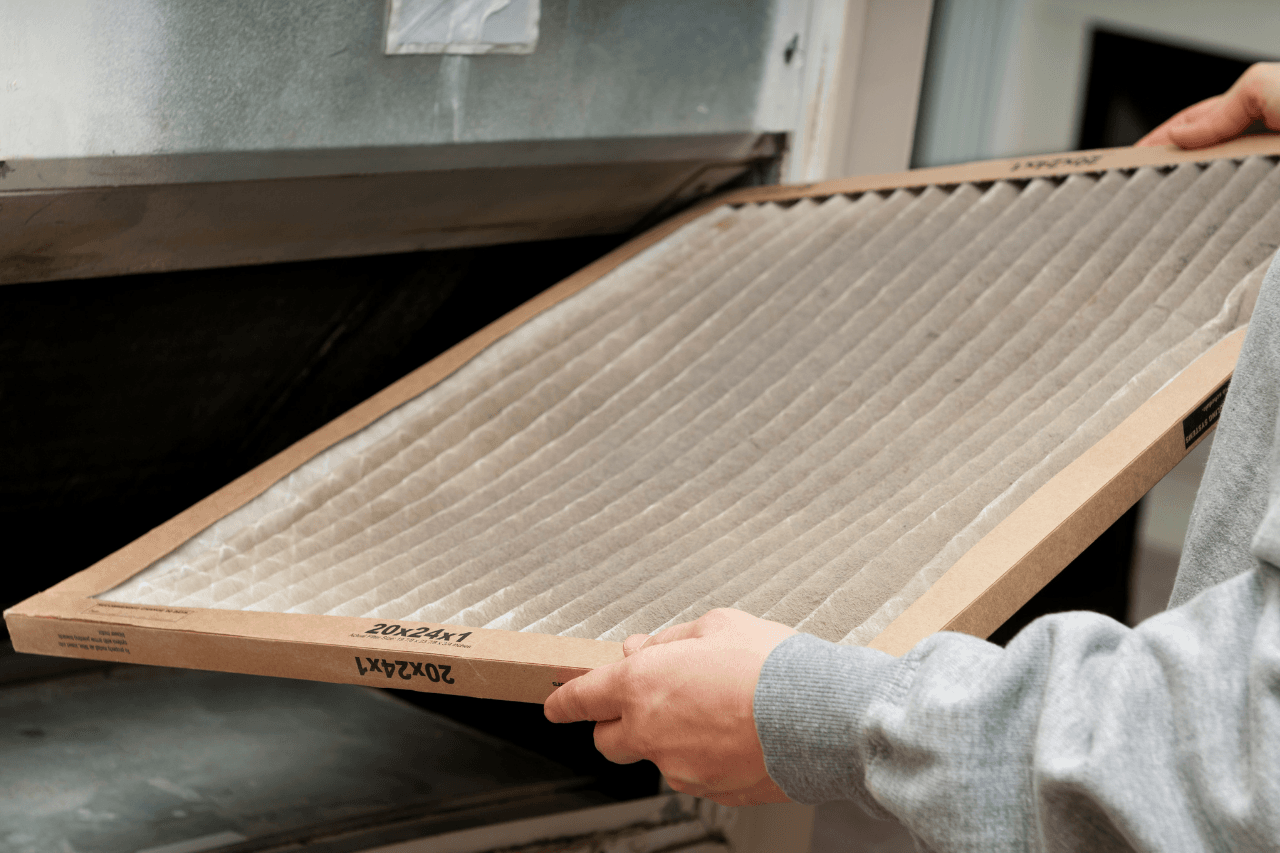 A man is holding an air filter in an air conditioning unit.