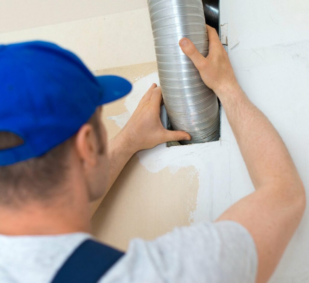 A man in a blue hat is installing a pipe in a wall.