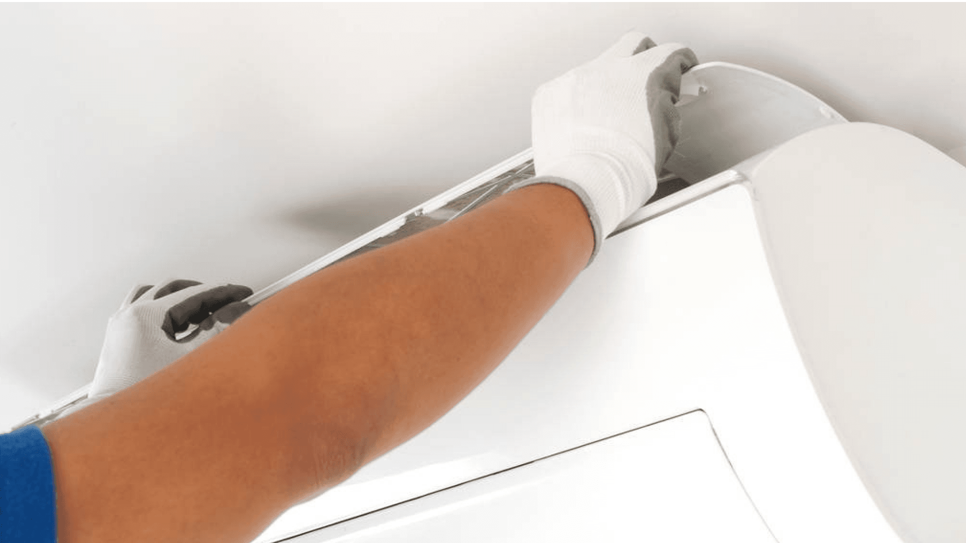 A person in blue gloves is fixing a white air conditioner.