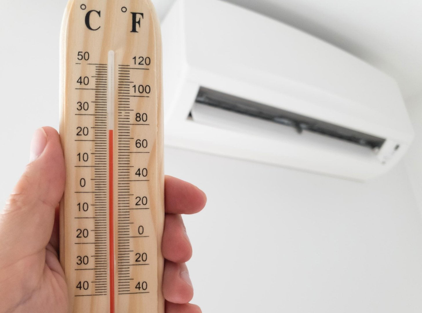 A hand holding a thermometer next to an air conditioner.