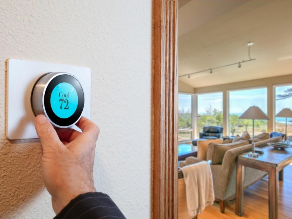 A person holding a smart thermostat in a living room.