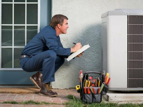 A man is kneeling down next to an air conditioner.