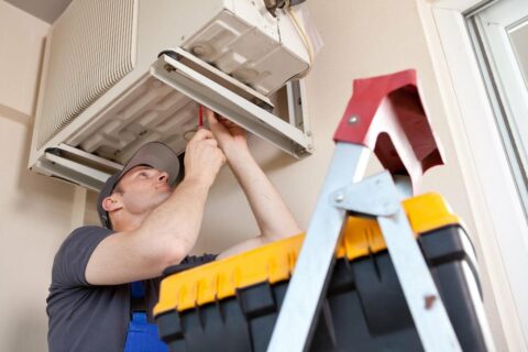 A man fixing an air conditioner in a room.