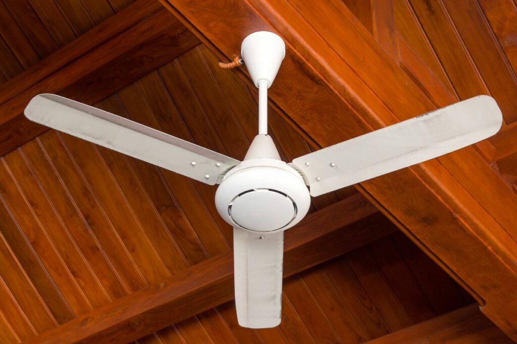 A white ceiling fan on a wooden ceiling.