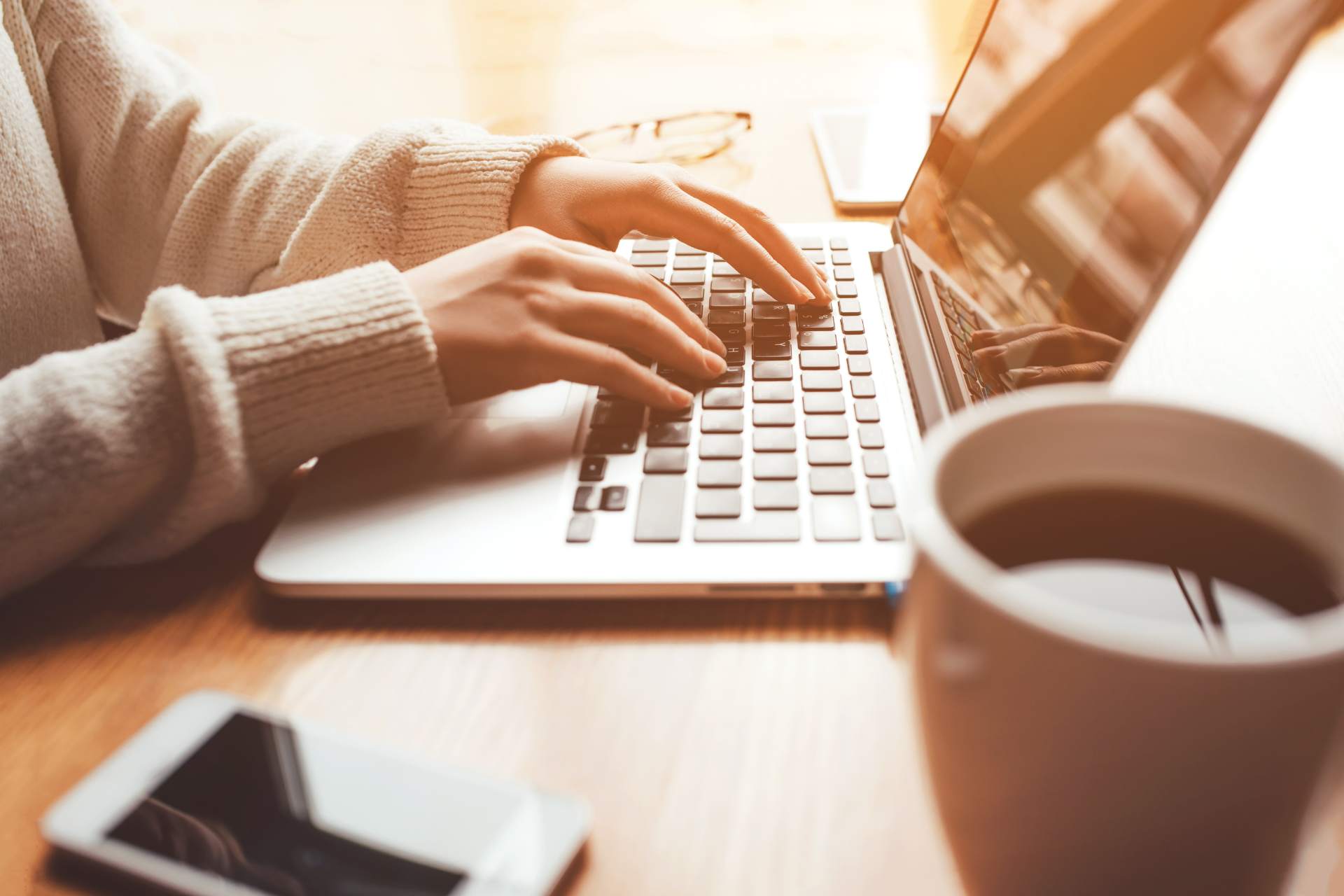 A woman in contact with her work, typing on a laptop with a cup of coffee.