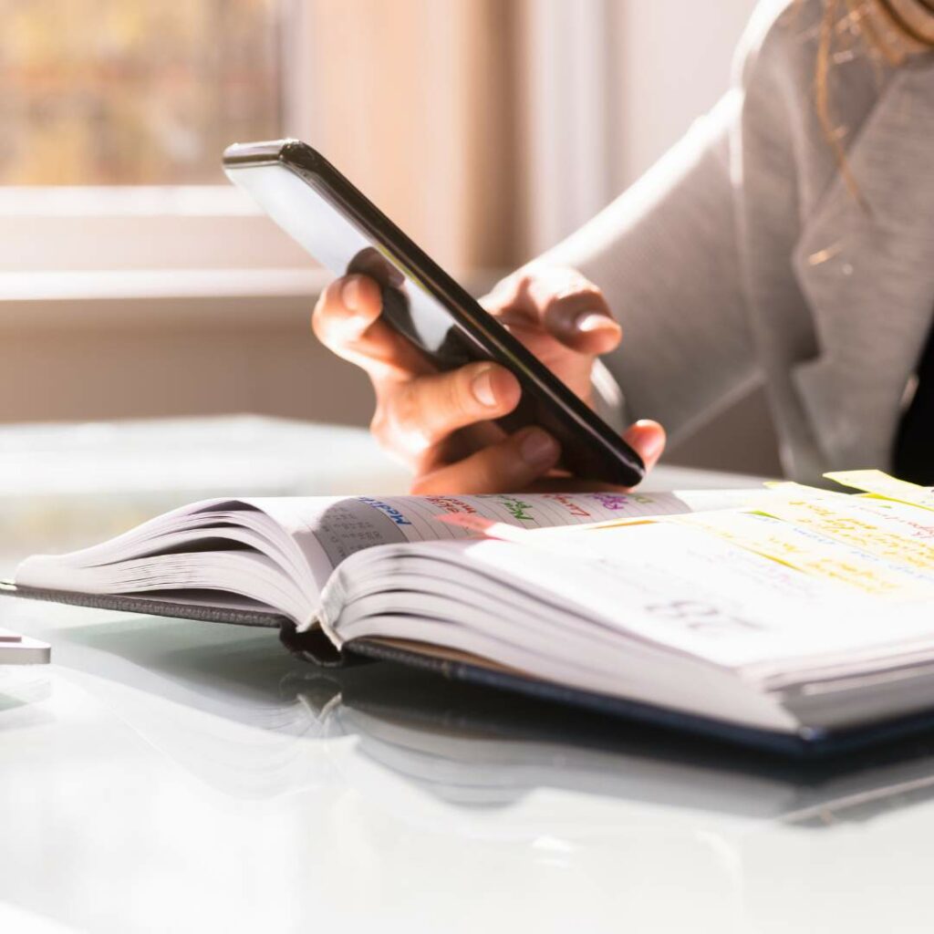 A woman multitasking with a smartphone and a book.