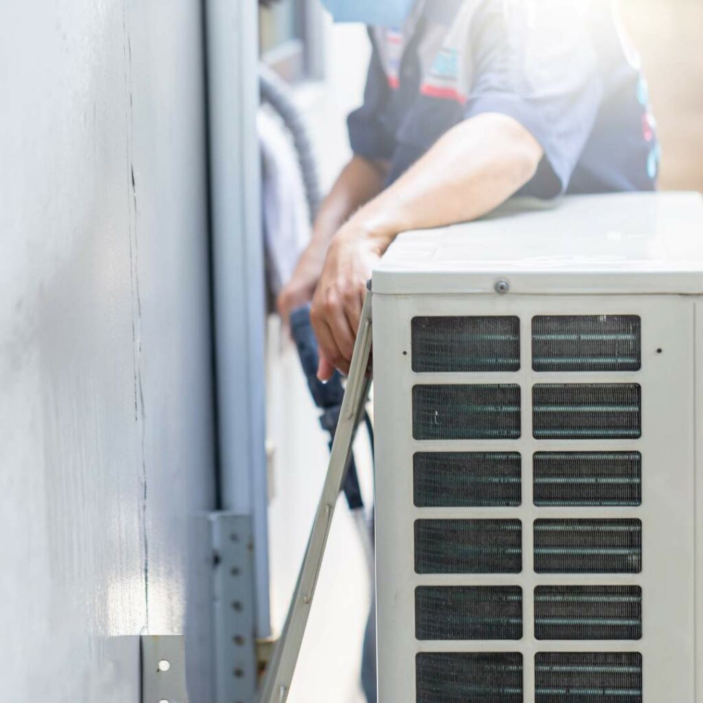 A man is repairing an air conditioner on the side of a building using commercial hvac services.