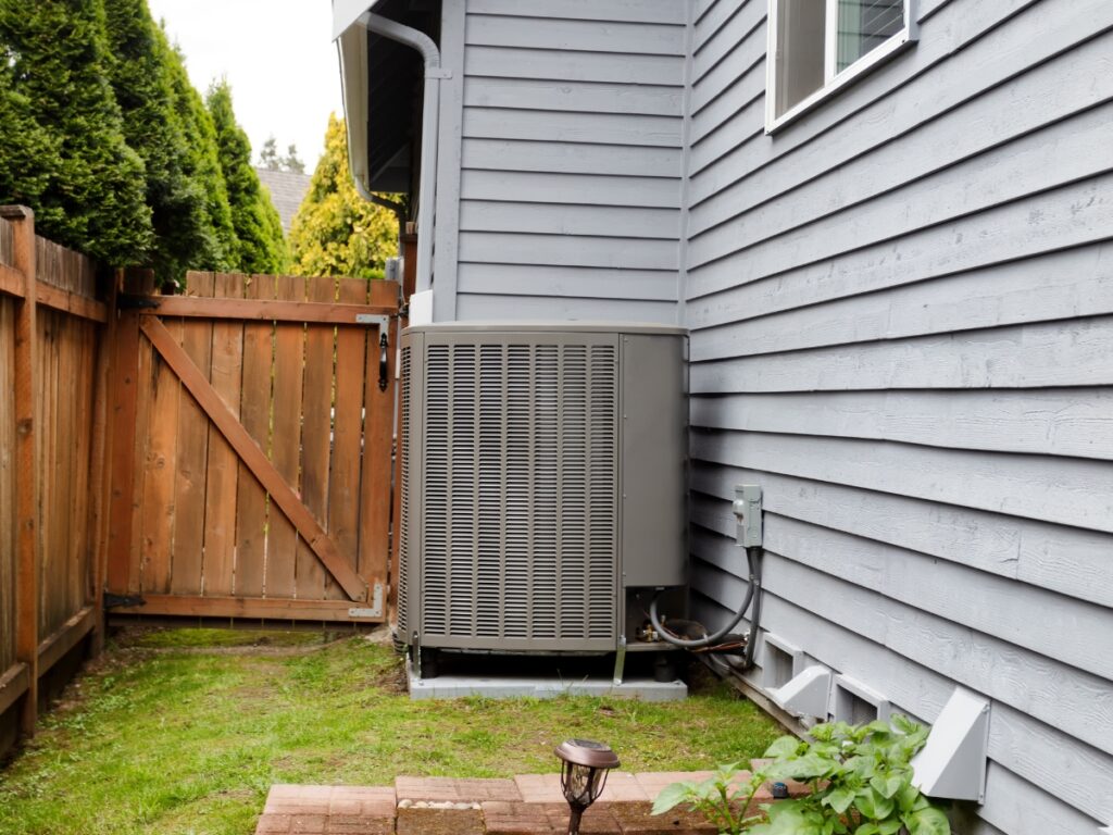 A grey air conditioner condenser fan not running outside of a house.