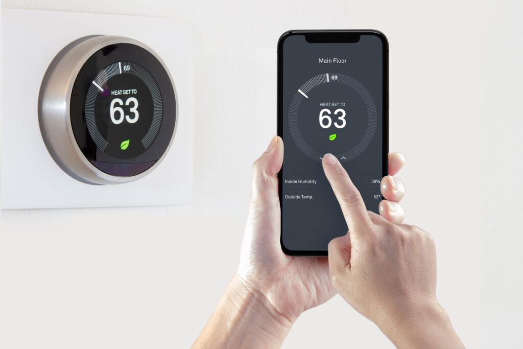 A person using a smartphone to control a wireless thermostat.