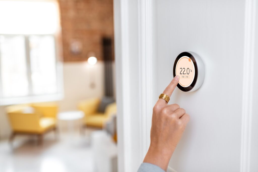 A woman is pointing at a wireless thermostat in a room.