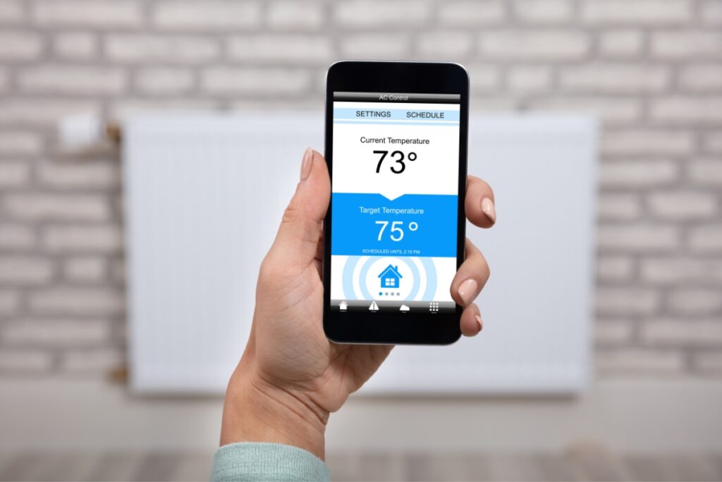 A woman holding a smart phone with a wireless thermostat on it.