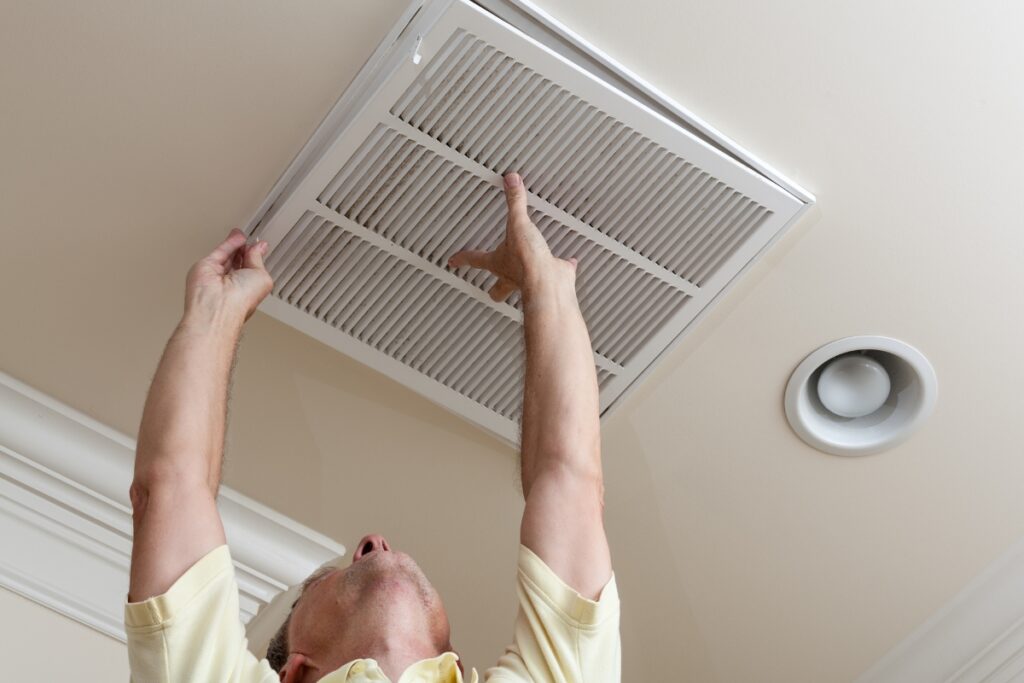 A man is holding up an air conditioner and showing signs you need to change your home air filter.