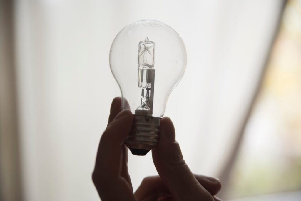 A person holding a light bulb in front of a window to check signs indicating the need to change your home air filter.