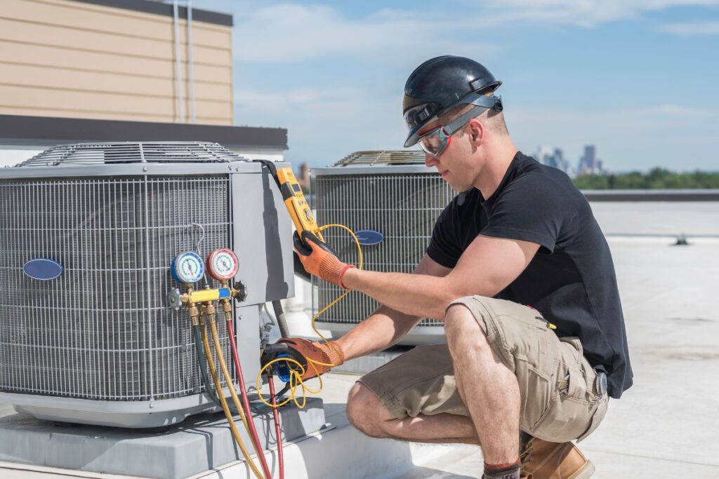 A man inspecting and servicing an air conditioning unit on a roof.