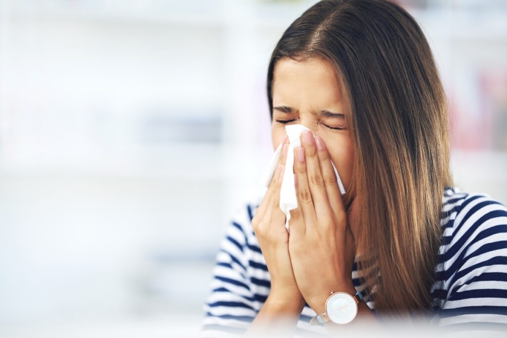 A woman blowing her nose, indicating the need to change your home air filter.