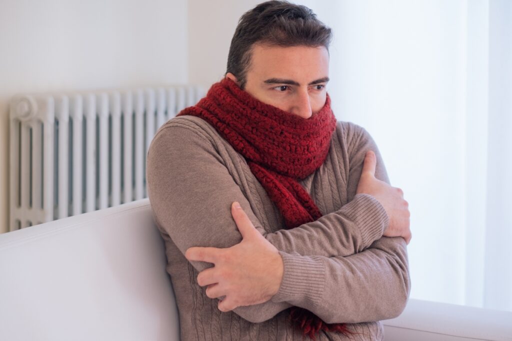 A man in a red scarf sitting on a couch during winter, contemplating what to do if he loses heat.