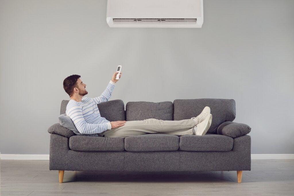 A man sitting on a couch, enjoying the cool breeze from a wireless thermostat and receiver linked to an air conditioner.