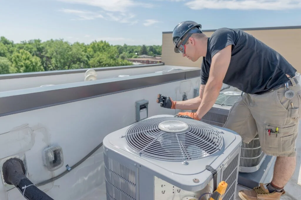 A man enhancing energy efficiency while working on an air conditioner on a roof.