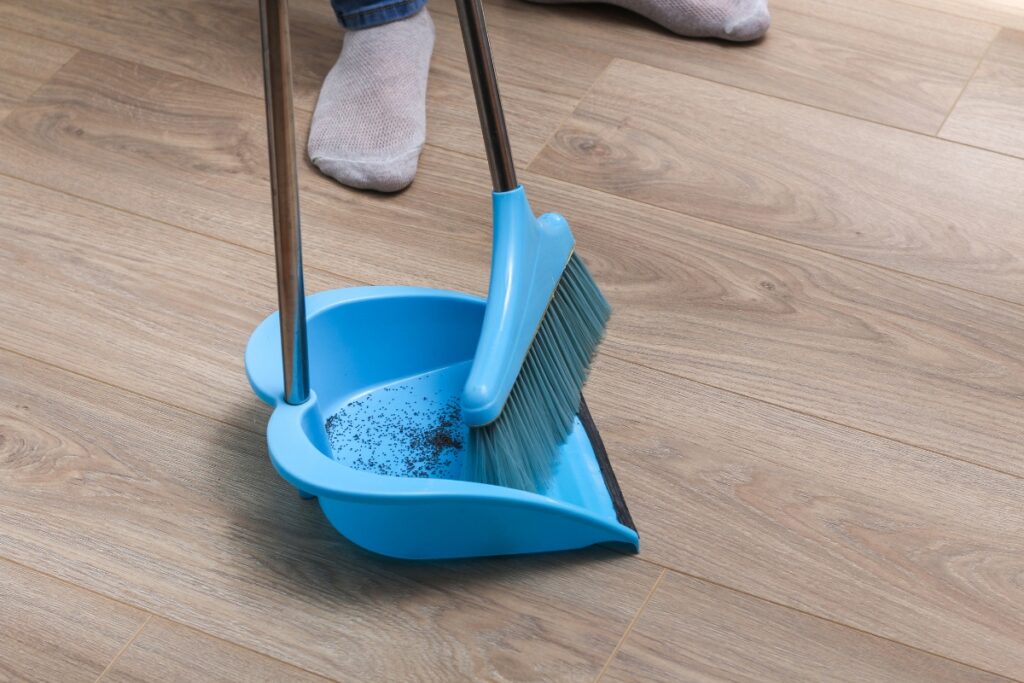 A woman is sweeping a floor indoors using a blue broom, ensuring efficient cleaning and maintaining good indoor air quality.