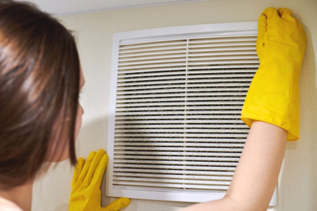 A woman ensuring indoor air quality while cleaning a duct with yellow gloves.