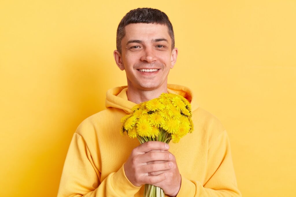 A young man holding a bunch of yellow flowers on a bright yellow background.
Keywords: yellow, flowers