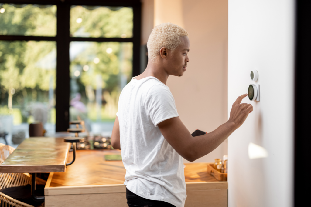 A man in a white shirt is checking on a smart thermostat on a wall.