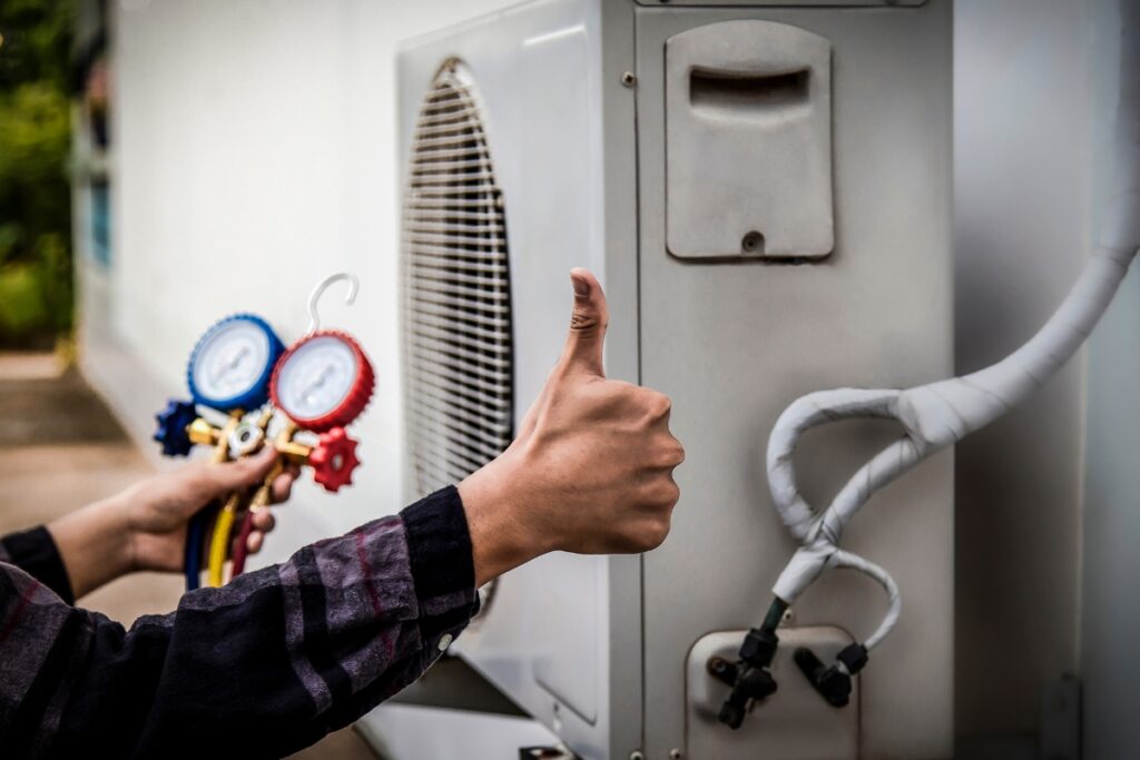 A technician gives a thumbs-up while checking a new AC unit with a gauge manifold attached.