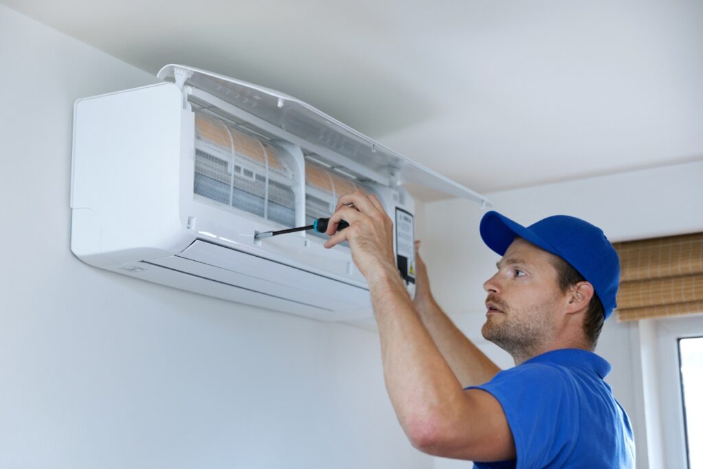 A technician in a blue cap installing a new AC unit, potentially increasing home value, mounted on a white wall.