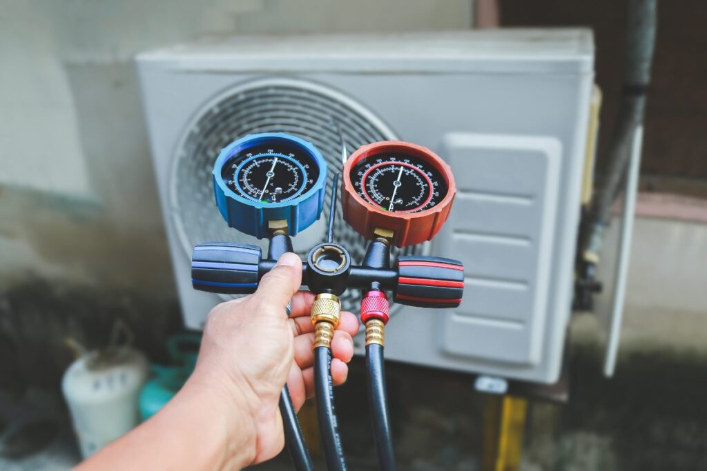 A person's hand holding pressure gauges connected to a new AC unit, potentially increasing home value and ensuring maintenance.