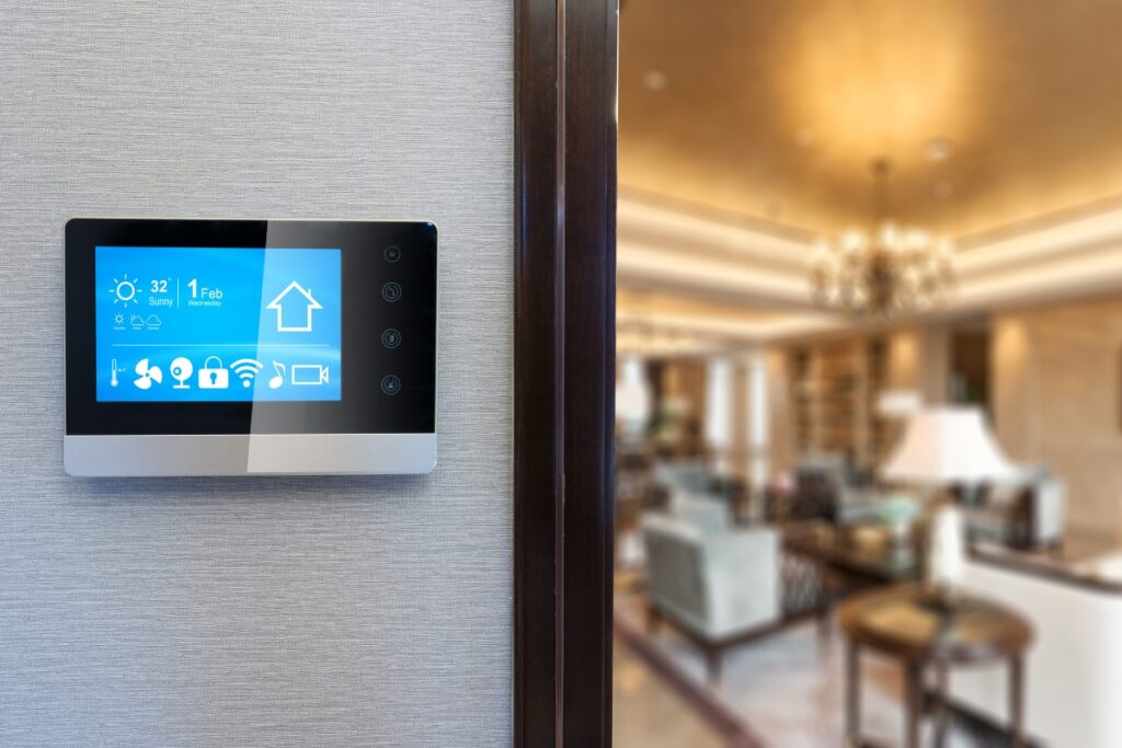 A smart home control panel mounted on a wall displays temperature and various control options powered by emerging HVAC technologies. In the background, a modern, warmly lit living room is visible.