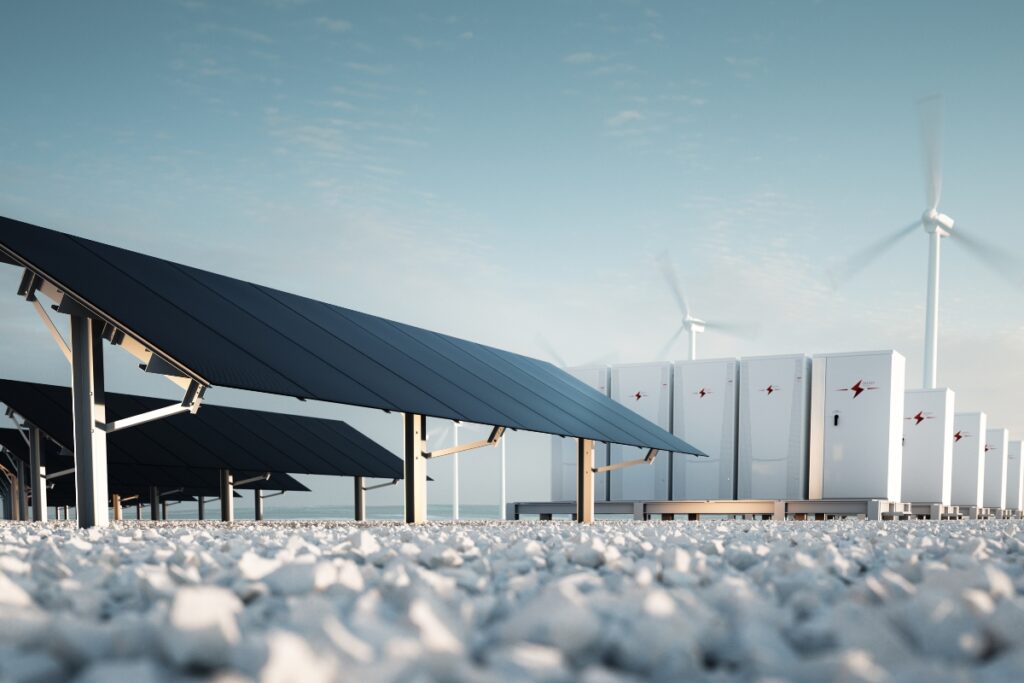 A solar farm with large solar panels in the foreground, battery storage units, and wind turbines in the background against a clear sky highlights the integration of renewable energy systems.