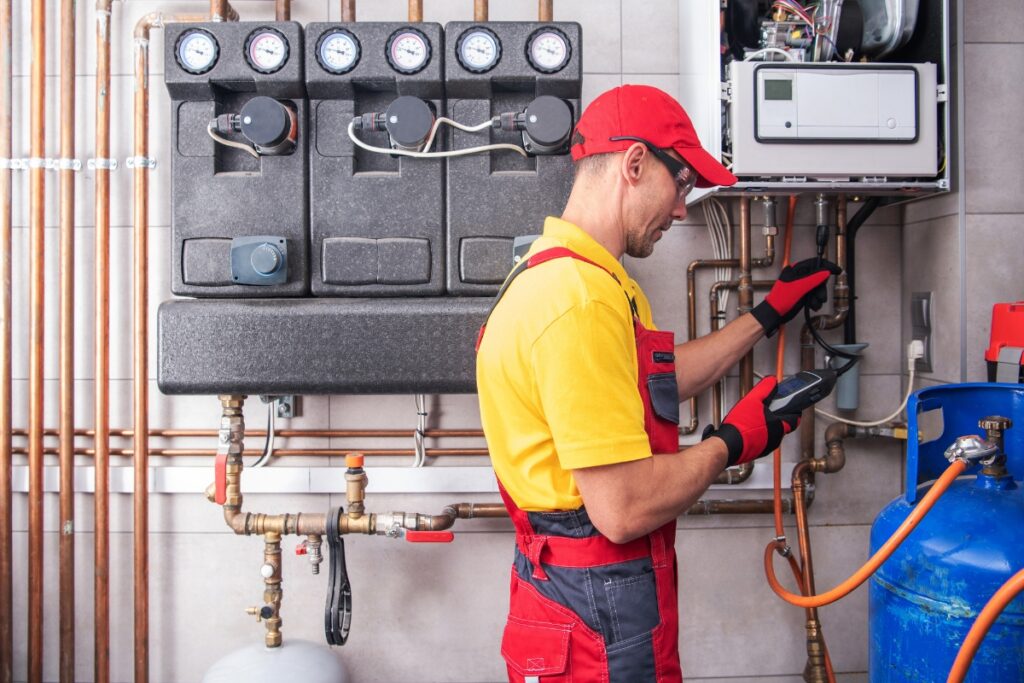 A technician in red and yellow uniform inspects industrial equipment with gauges and pipes, holding a device and wearing gloves and a cap, ensuring the hvac system integrates well with renewable energy systems.