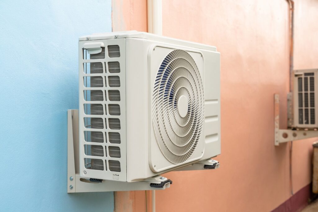 An outdoor air conditioning unit, part of advanced HVAC renewable energy systems, is mounted on a blue and beige wall.