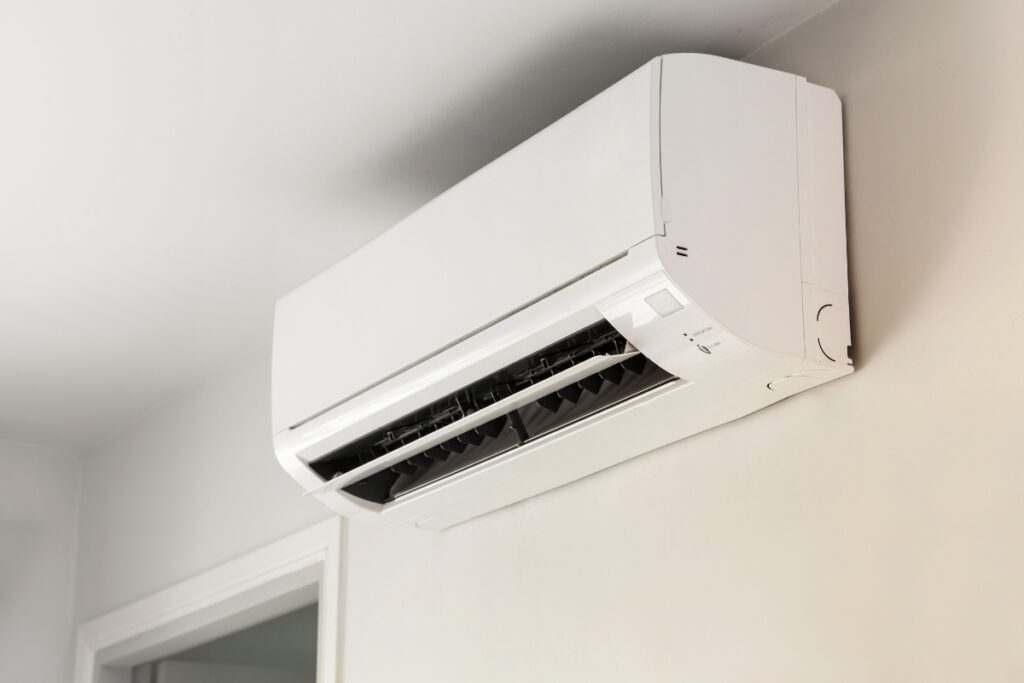 A white, wall-mounted air conditioner is installed near the ceiling in a room with light-colored walls. The unit has an open vent ready for operation, offering health benefits of air conditioning by maintaining optimal indoor temperatures and improving air quality.