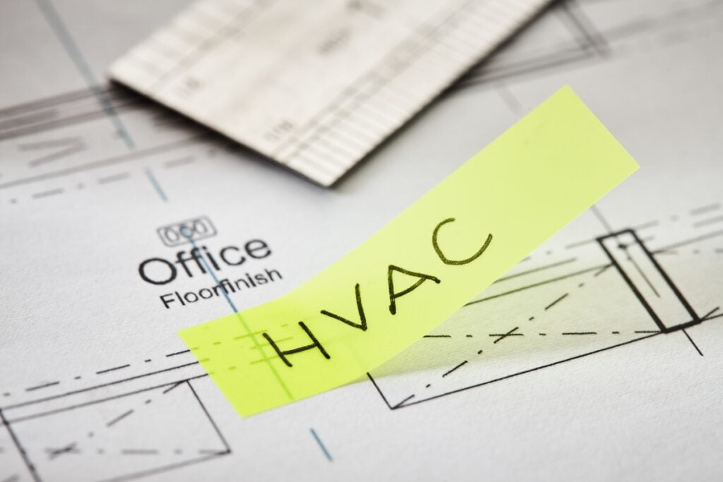 Close-up of an architectural floor plan with a yellow sticky note labeled "HVAC" placed on top, highlighting the detailed aspects of HVAC planning.