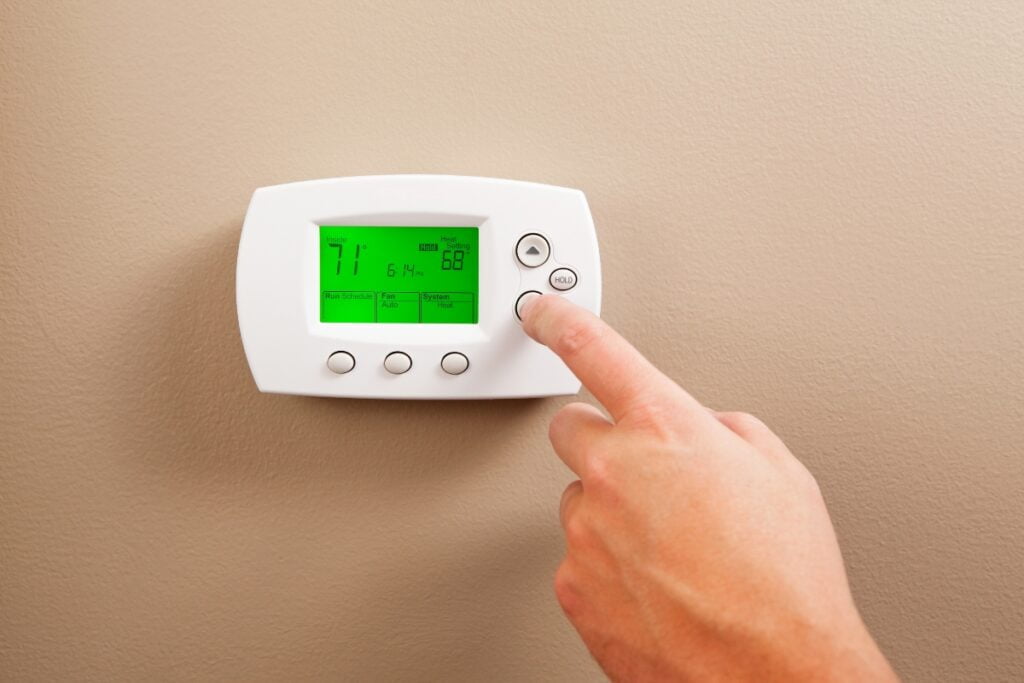 A hand adjusting the settings on a digital thermostat, a key part of hvac planning, mounted on a beige wall, displaying a temperature of 71°F.