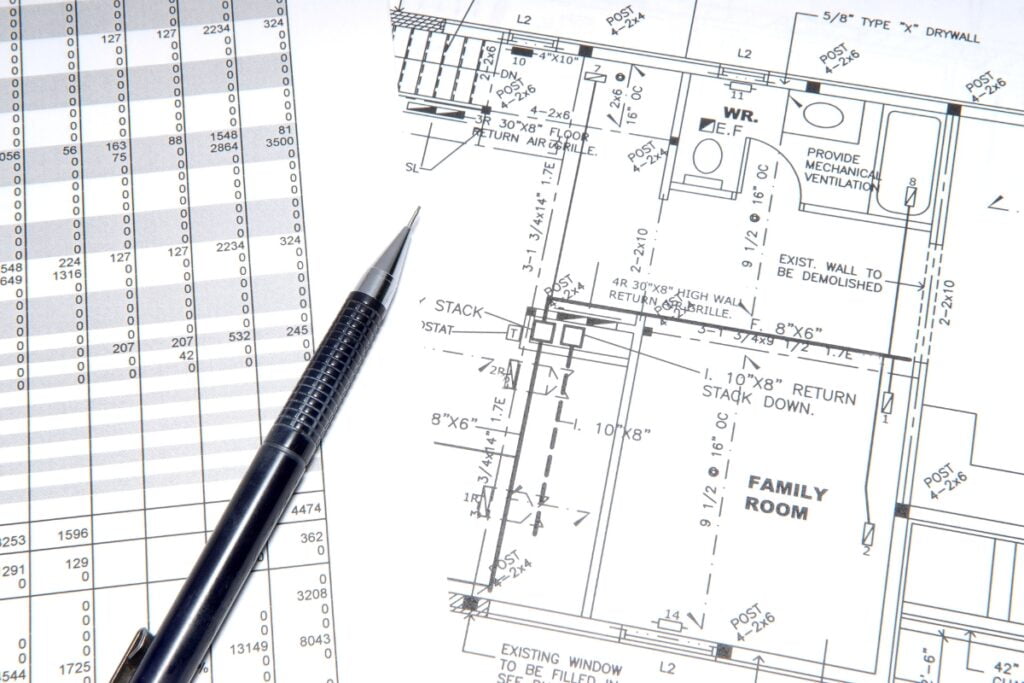 Close-up of architectural blueprints with a pen placed on top, showing detailed plans for a family room, surrounding areas, and HVAC planning. There is also a spreadsheet visible next to the blueprints.