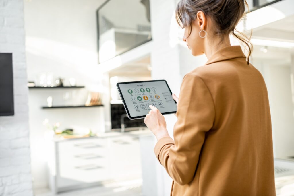 A woman in a brown blazer uses a tablet to control smart home devices in a modern kitchen, seamlessly integrating HVAC planning into her daily routine.