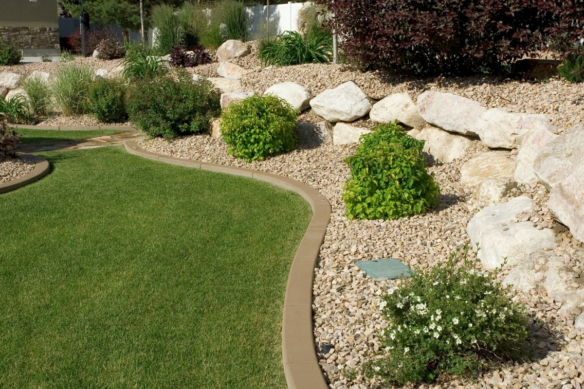 A landscaped garden with a curved lawn border, various shrubs, and plants surrounded by rocks and mulch provides not only beauty but also hvac landscaping benefits for energy efficiency.