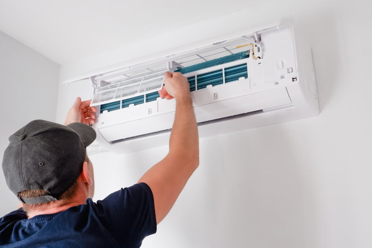 A person wearing a cap is performing maintenance or installation on a wall-mounted air conditioning unit, showcasing the precision and expertise often seen in HVAC emergency services.