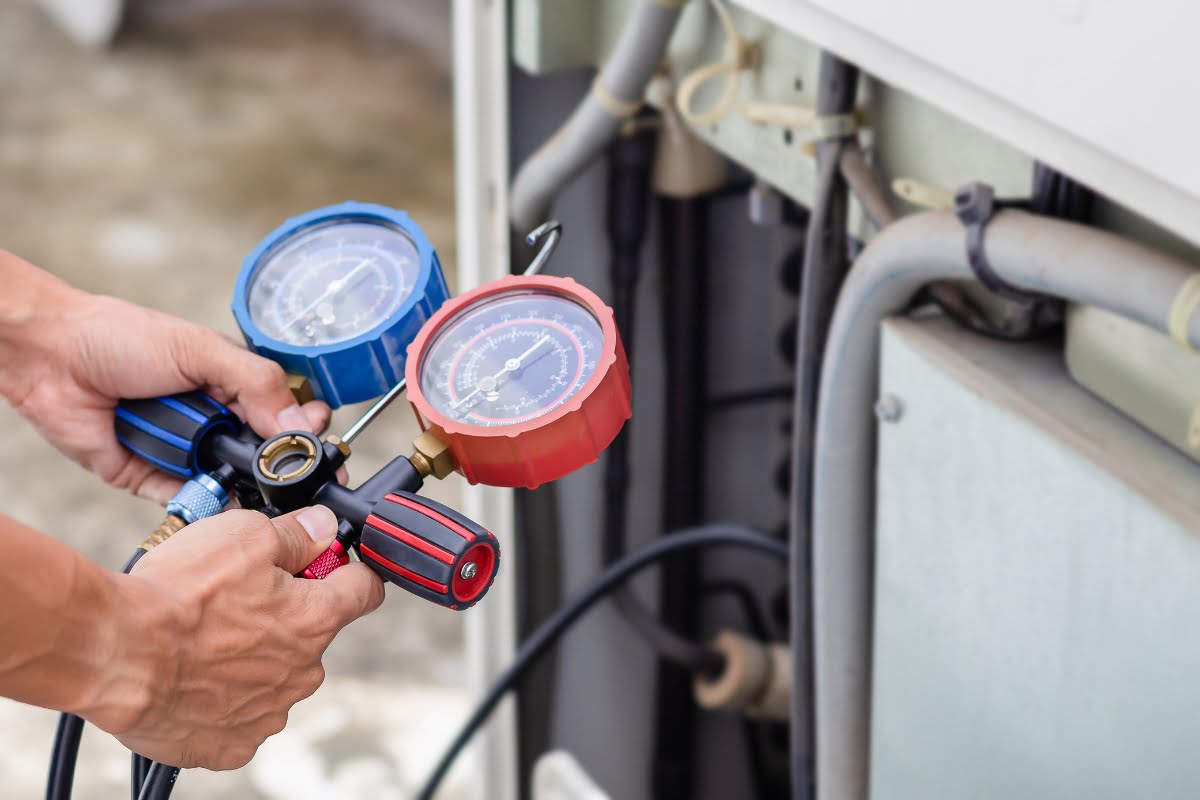 A person holds and adjusts pressure gauges attached to air conditioning equipment for maintenance or repair work, ensuring rapid response as part of HVAC emergency services.