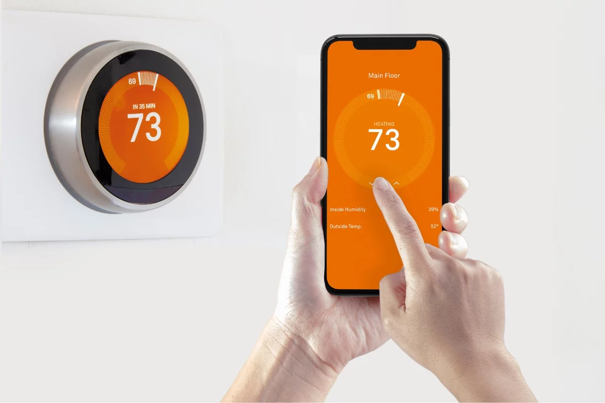 A person is adjusting a smart thermostat with a smartphone app, both displaying a temperature setting of 73 degrees, demonstrating the efficiency of modern HVAC energy solutions.