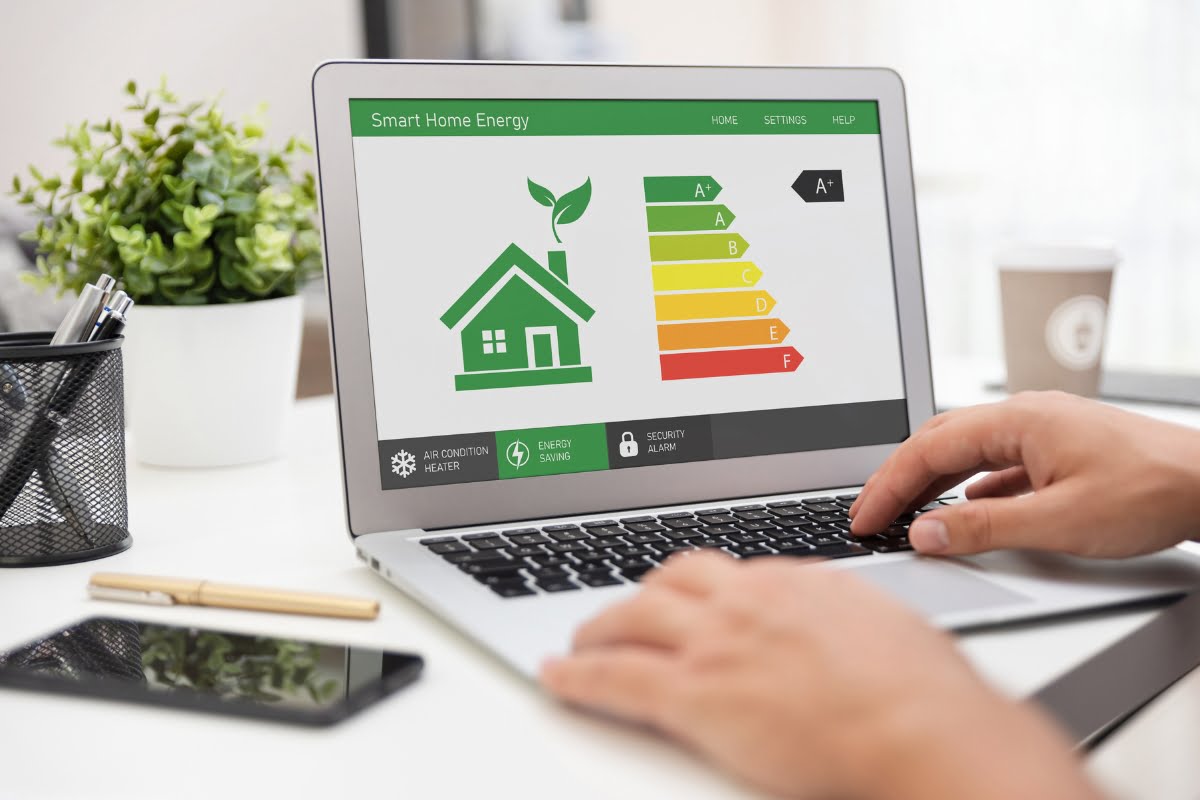 A person is using a laptop displaying a smart home energy monitoring interface, featuring an energy efficiency rating chart from A to G on the screen. The interface seamlessly integrates HVAC energy solutions for optimal performance.