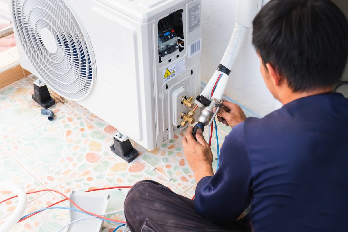 A person is expertly handling an HVAC real estate inspection, carefully installing or repairing the air conditioning unit while connecting wires and cables with precision.